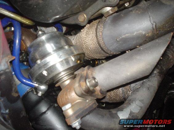 Close-up of a turbocharger wastegate connected to exhaust piping, with heat wrap visible