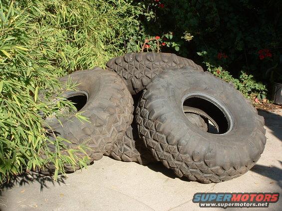 three large off-road tires stacked on concrete next to bamboo