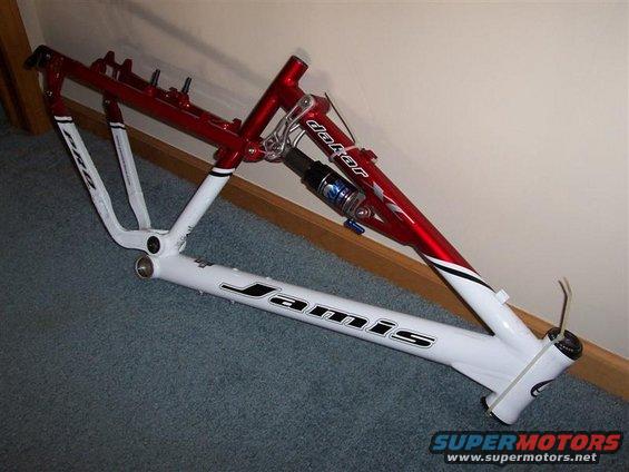 Red and white bicycle frame with 'Jamis' and 'Dakar' labels. Has a rear shock absorber