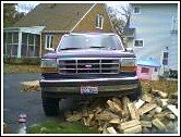 Front view of a dark-colored Ford Bronco parked on a pile of firewood
