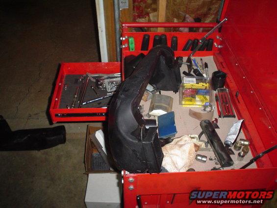 Red toolbox with an open drawer full of tools and a black car part on top. Some other parts and a tube of grease are also visible
