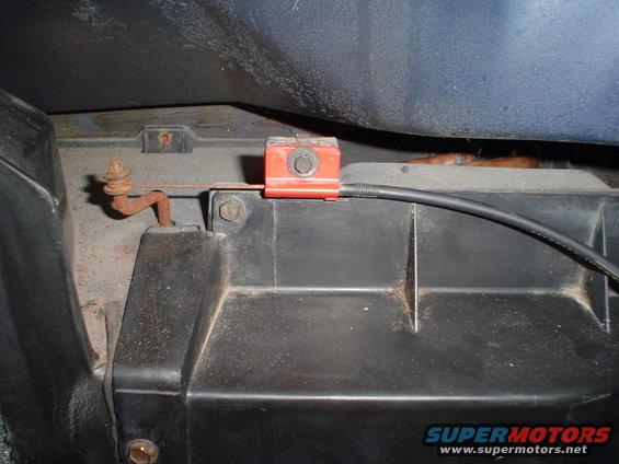 Interior car part with red bracket, bolt, and black cable attached to rusty metal