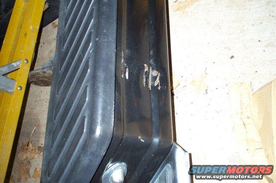 Close-up of a black truck fender with some scuffs and a textured running board next to it. A yellow ladder is visible on the left