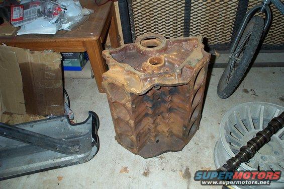 Rusty V8 engine block sitting on concrete floor next to a bicycle wheel and car part