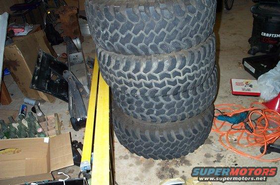 stack of four large off-road tires in a garage with tools and boxes