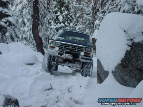 1986 Ford Bronco driving through deep snow on a wooded trail