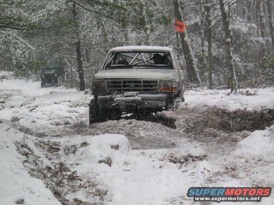White 1995 Ford Bronco with roll cage navigating snowy terrain