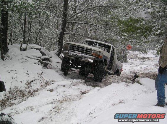 1995 Ford Bronco with roll cage driving through snow and rocks