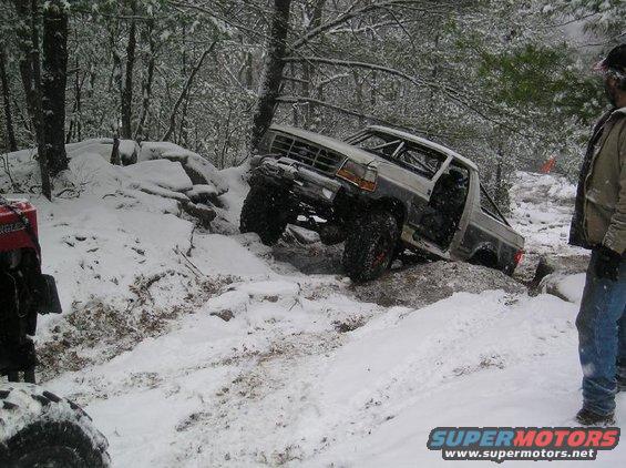 Off-road truck navigating snowy terrain with one wheel lifted