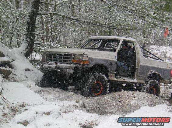 Silver Ford Bronco with roll cage, off-roading in snow
