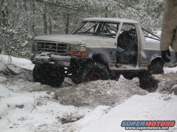1995 Ford Bronco with roll cage driving through snow and mud