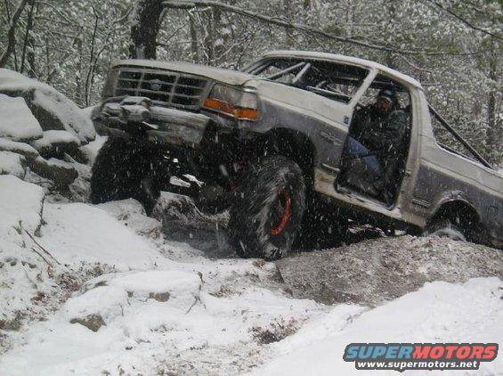 1995 Ford Bronco with roll cage driving over rocks in snow