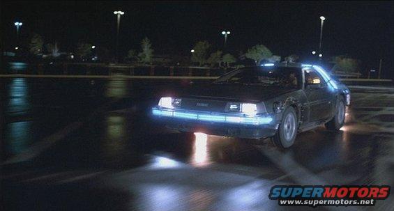 DeLorean DMC-12 with glowing blue lights, driving at night on a wet surface
