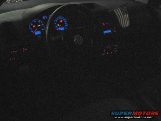 Dashboard of a 2002 Volkswagen Polo with blue-lit gauges and an American flag on the dash