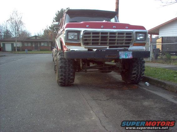 Front view of a lifted red and white Ford F-Series truck with large tires. License plate reads YFP 471