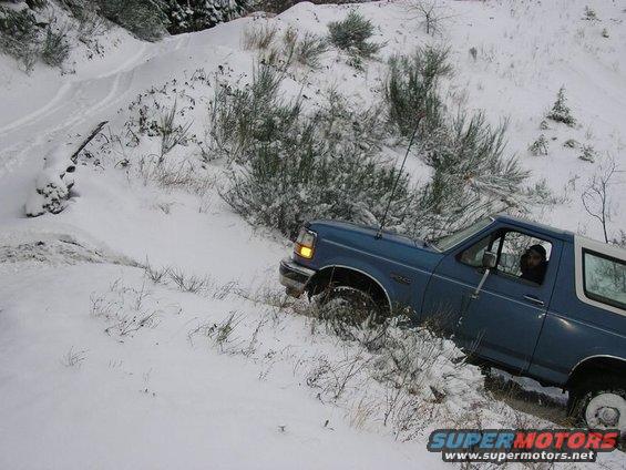 Blue 1992 Ford Bronco driving on a snowy, wooded trail
