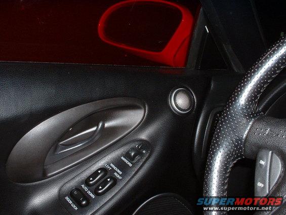 Interior door panel with window and mirror controls, speaker, and perforated steering wheel