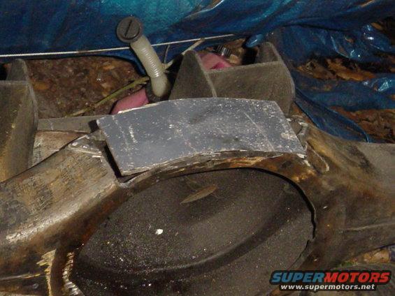 Close-up of a gray, curved metal piece over a dark, circular object, possibly a tire, under a blue tarp