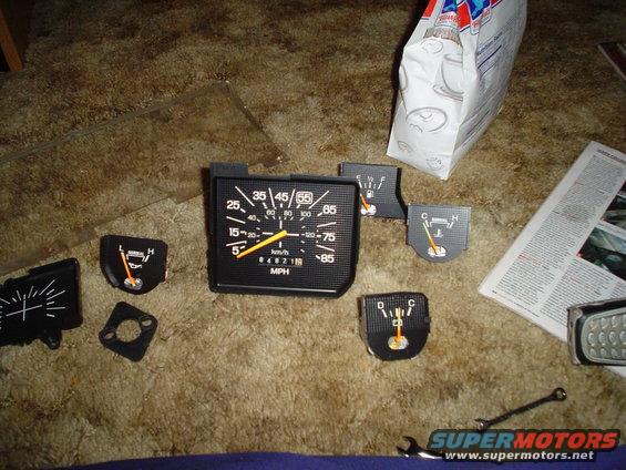 Dashboard gauges including a speedometer, fuel gauge, and temperature gauge laid out on a carpeted surface
