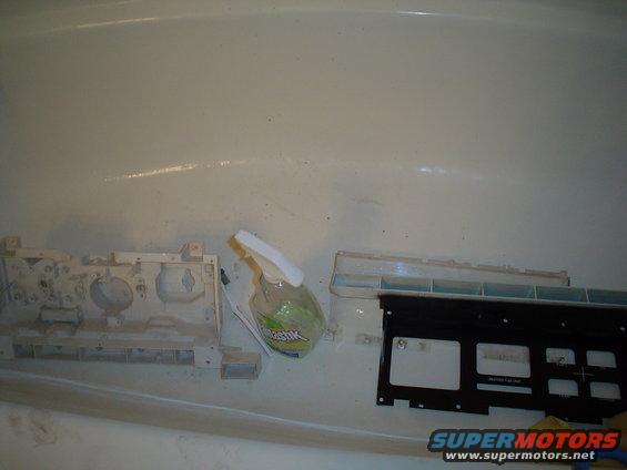 Car dashboard components and a spray bottle sitting in a bathtub