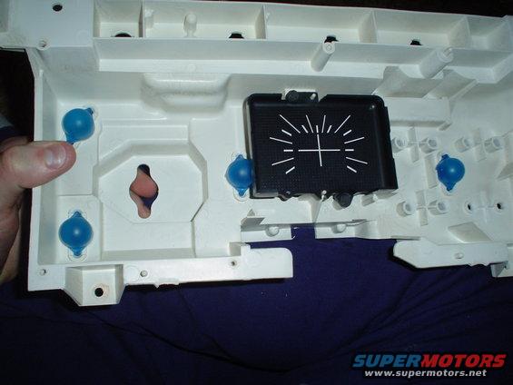 White plastic dashboard gauge cluster housing with a black gauge face showing radial lines and a crosshair