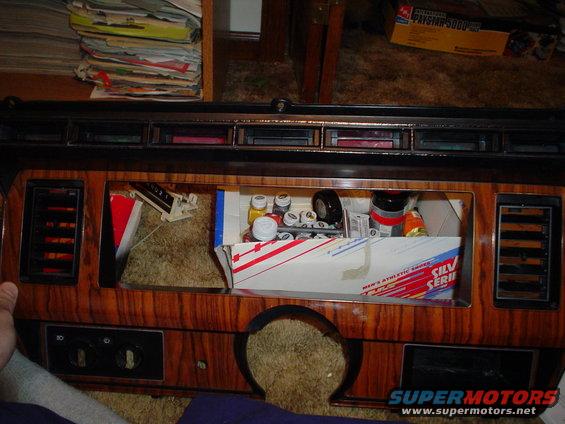 Dashboard with wood grain trim, open cubby filled with parts and a box of athletic shoes