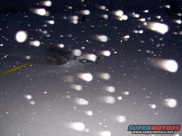 Vehicle driving through snow with lights on, possibly at night