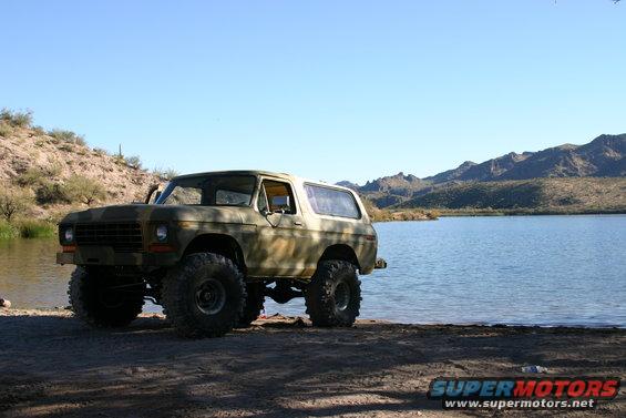 Camouflaged 1978 Ford Bronco with large tires parked by a lake