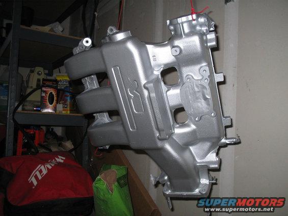 Silver painted intake manifold hanging by red string, with shelves and items in background