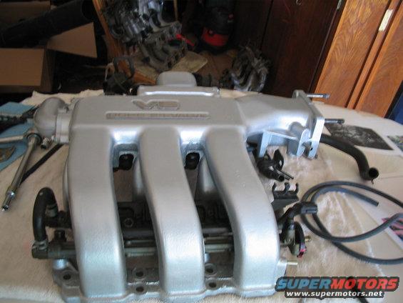 Silver V6 DOHC intake manifold with hoses attached, on a table