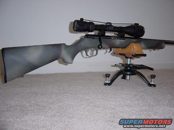 Camouflaged rifle with scope mounted on a black tripod rest