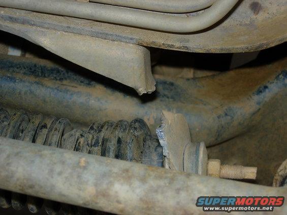 Close-up of a broken metal bracket attached to a vehicle's suspension spring