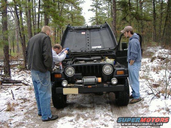 Three guys looking at a 1997 Jeep TJ with the hood open in a snowy wooded area