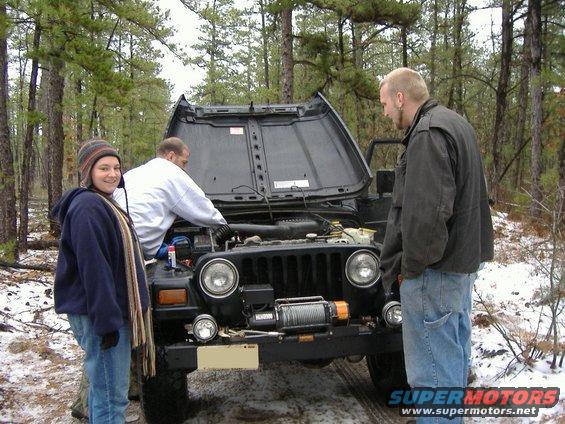 Black Jeep Wrangler with hood open, winch on front bumper, people working on engine
