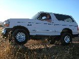 White Ford Bronco with lifted suspension and aftermarket wheels parked on a dirt road