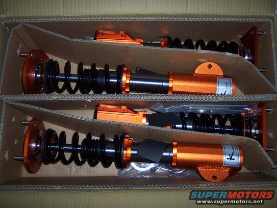 Two orange coilover suspension assemblies in a cardboard box