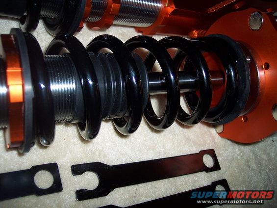 Adjustable coilover suspension parts with black springs and orange mounting hardware, along with adjustment wrenches