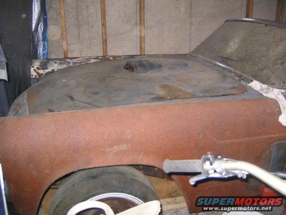 Rusty car hood and fender in a garage, with a motorcycle handlebar visible