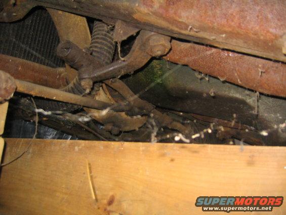 Undercarriage of a rusty car with visible suspension components and wooden planks below