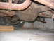 1956 Ford Thunderbird - Underside view of a vehicle's rear axle and suspension system, showing rusty components and a tire.