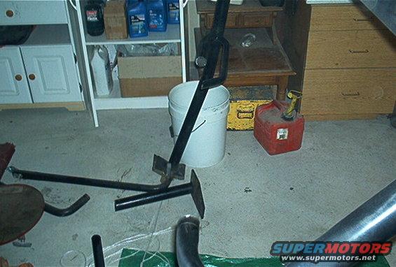 Automotive exhaust pipe section and a jack stand next to a white bucket and red gas can