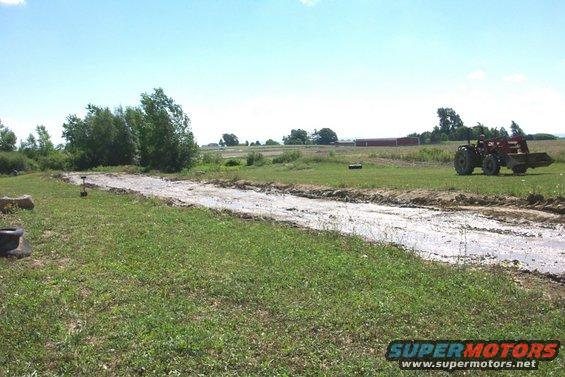 Tractor with front loader parked in a muddy field next to a dirt track