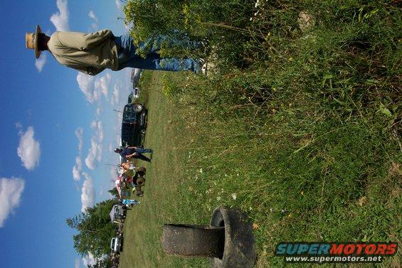 People and vehicles in a grassy field under a blue sky with clouds