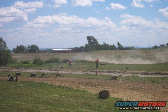 Truck kicking up dust on dirt track with two people watching