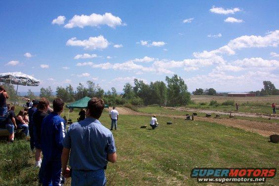People gathered outdoors on a sunny day with a field and trees in the background
