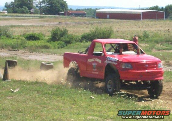 Red pickup truck with racing decals kicking up dirt