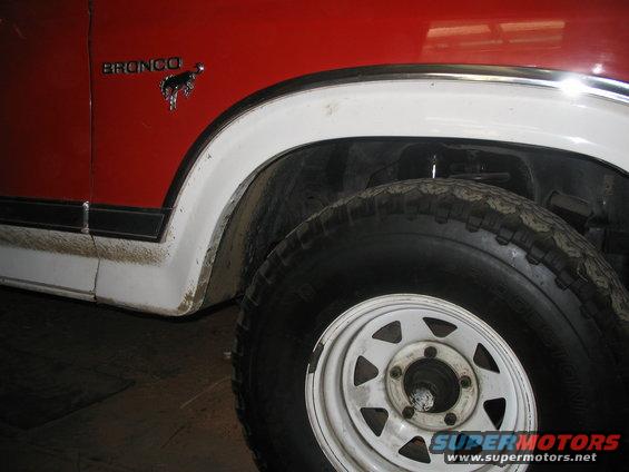 Red and white Ford Bronco fender with 'BRONCO' badge and horse emblem, showing a white steel wheel and tire