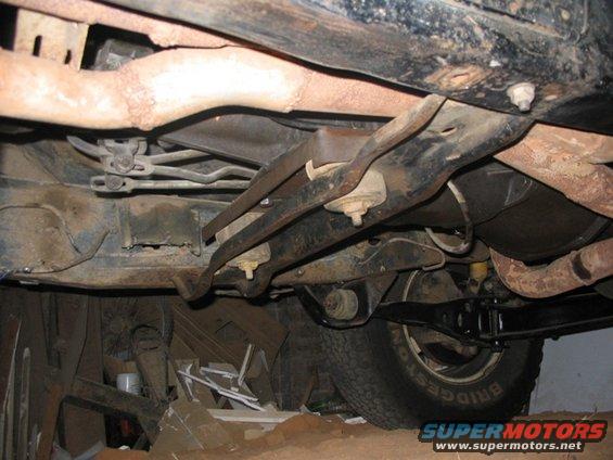 Underside of a vehicle with visible suspension components, exhaust pipes, and a tire with "BRIDGESTONE" text