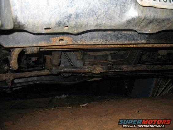 Underside view of a vehicle's steering and suspension components. Some rust is visible on the frame