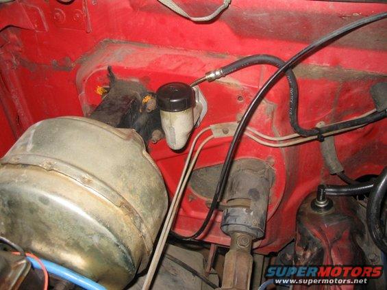 Close-up of brake master cylinder and booster assembly in a red engine bay